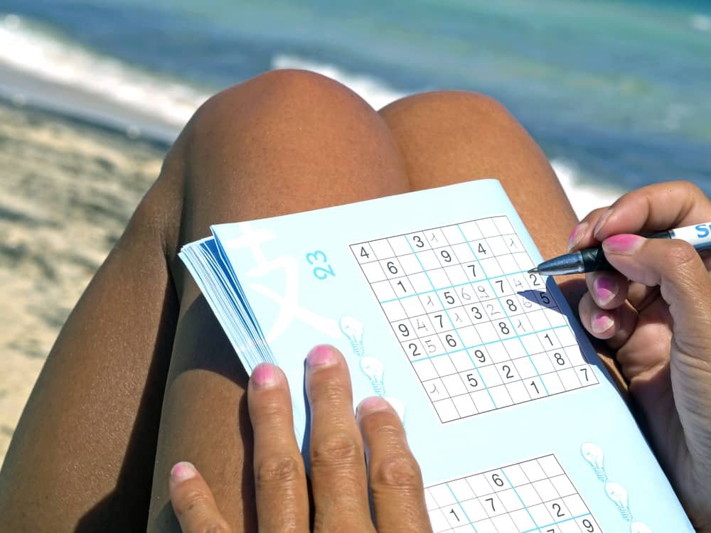 girl playing sudoku sitting on the seashore