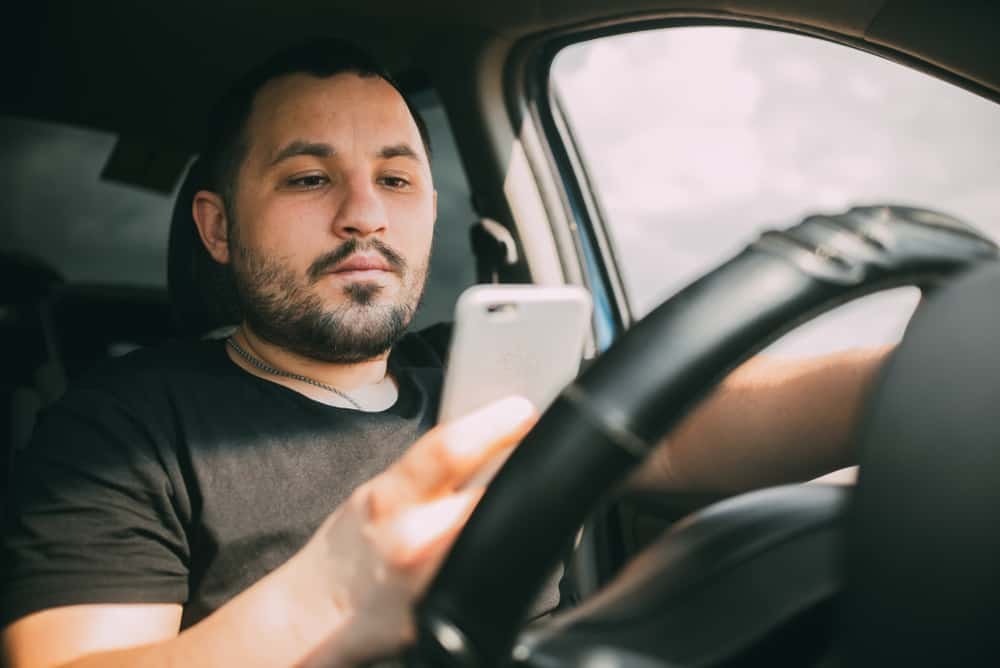 man driving a car distracted by a smartphone sudoku