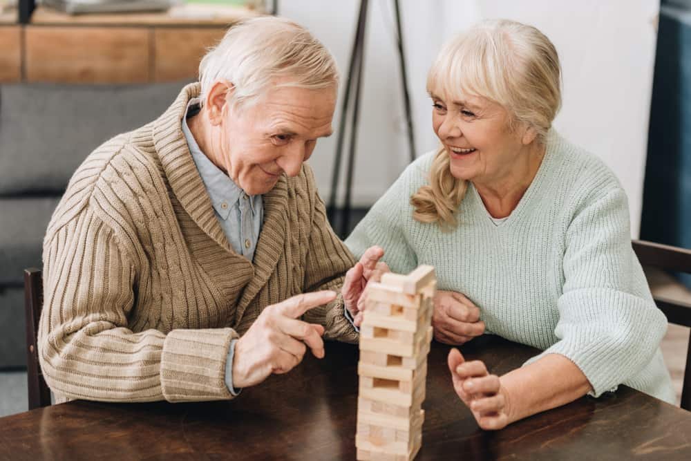 retired husband and wife playing jenga game on table