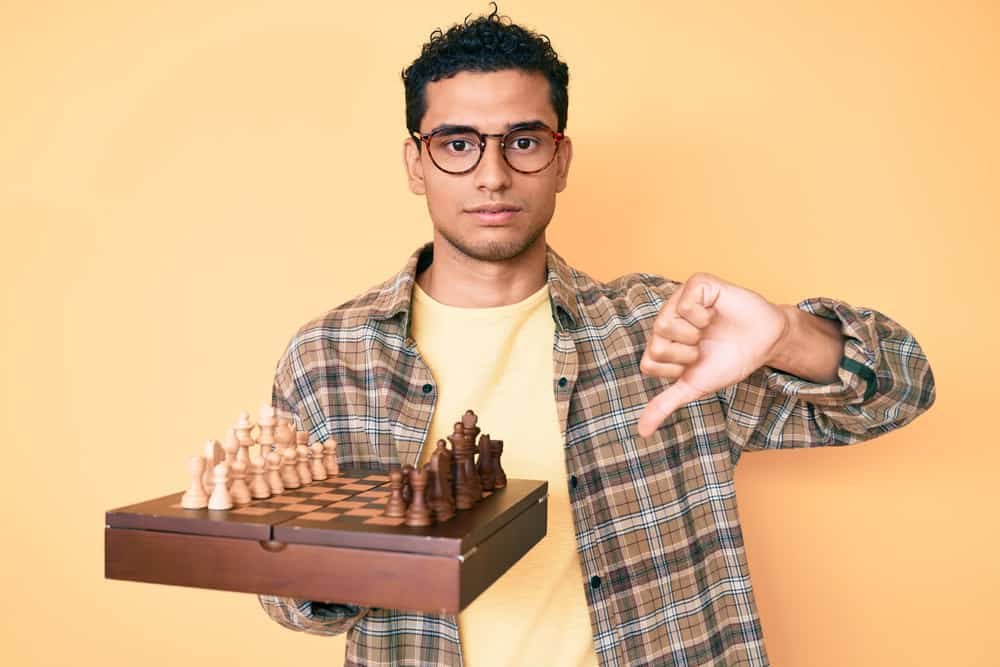 man holding chess board wearing glasses with angry face, negative sign showing dislike with thumbs down