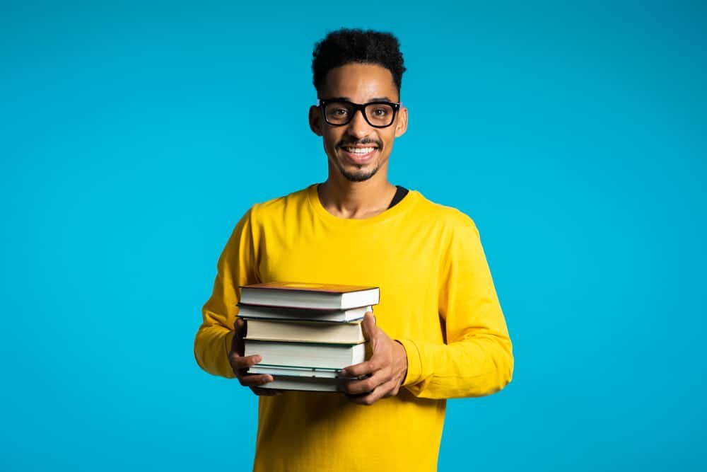 African student on blue background in the studio holds stack of university books