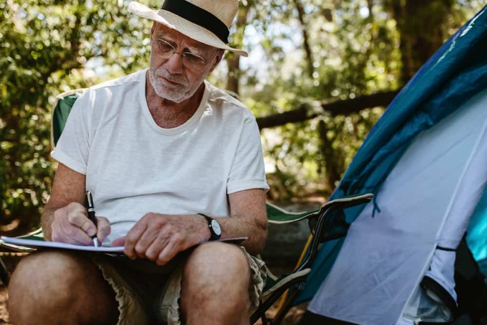 Senior man sitting in front of a tent and doing a word search puzzle