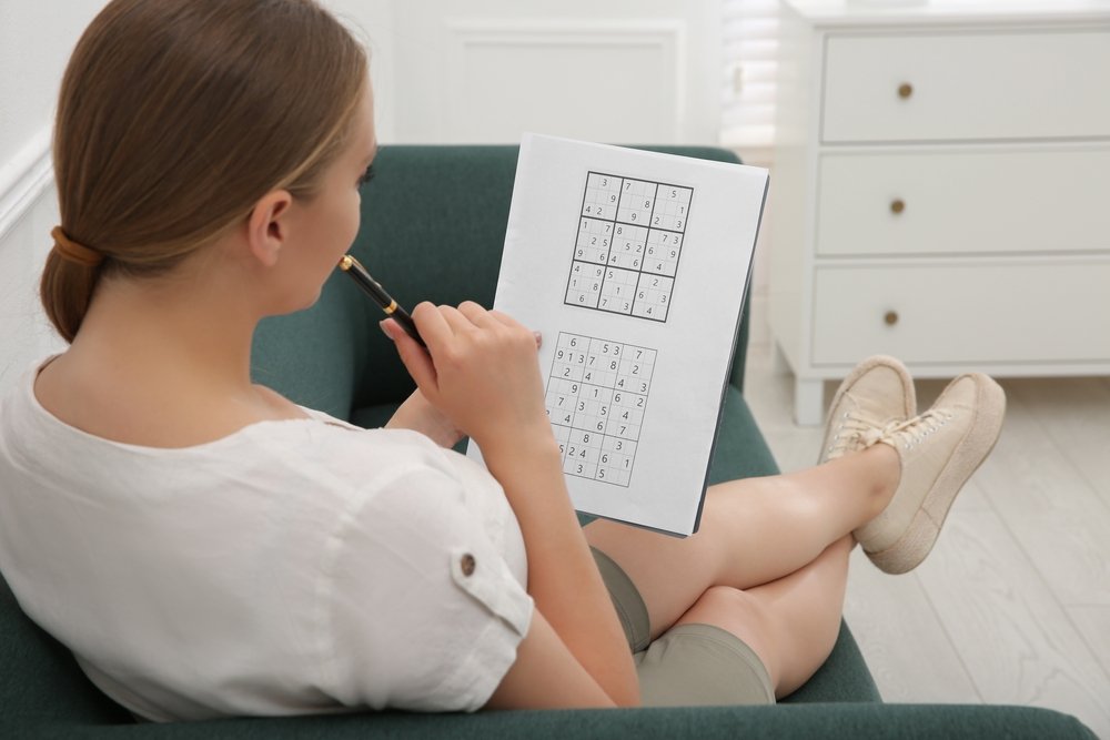 Young woman solving sudoku puzzle on sofa