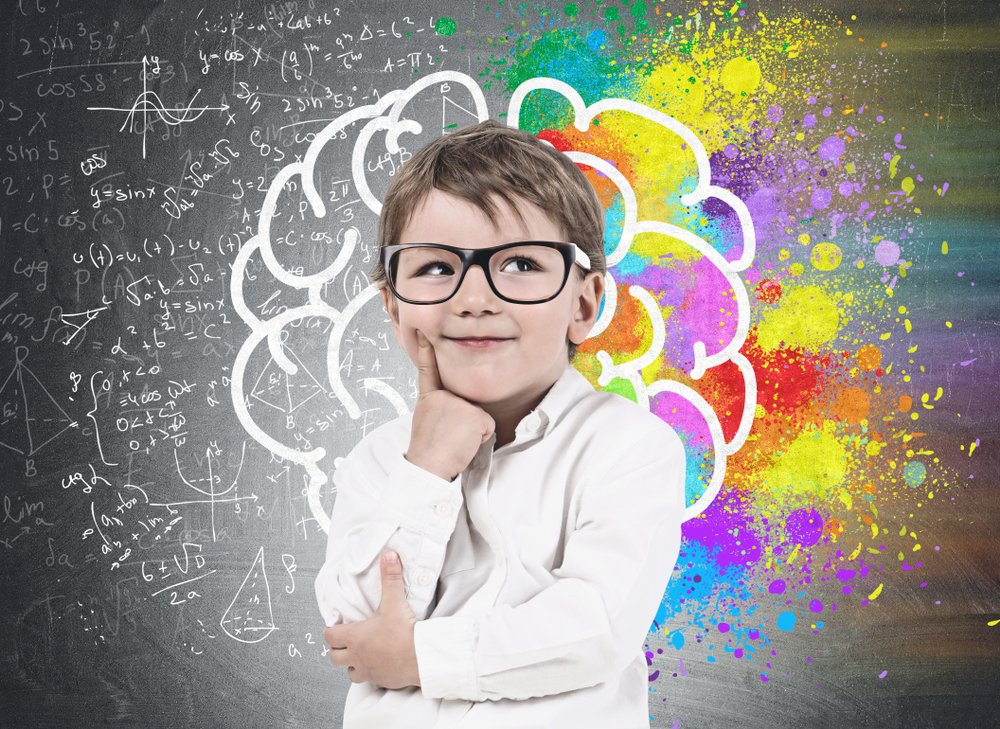 boy wearing white shirt and glasses standing near blackboard with colorful brain sketch