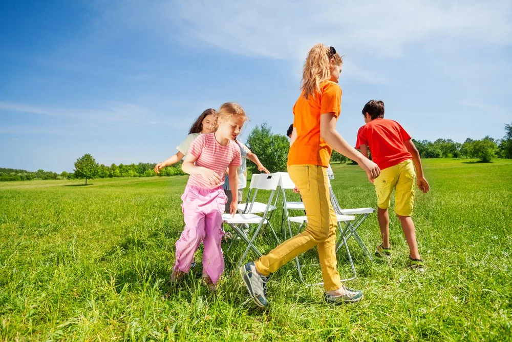 Children run around chairs playing a game outside
