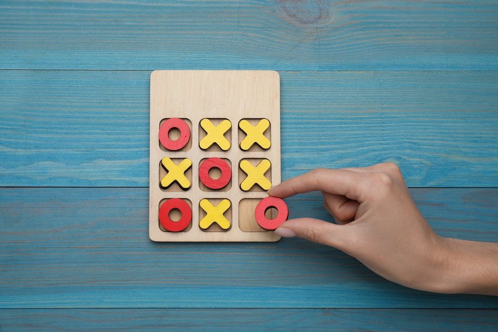 Woman playing tic tac toe game at light blue wooden table