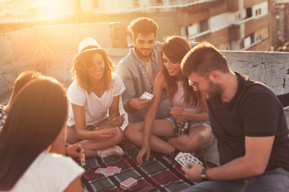 people sitting on a picnic blanket, having fun while playing cards