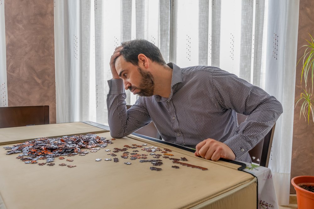 Bearded man in white and black shirt doing puzzle in his living room
