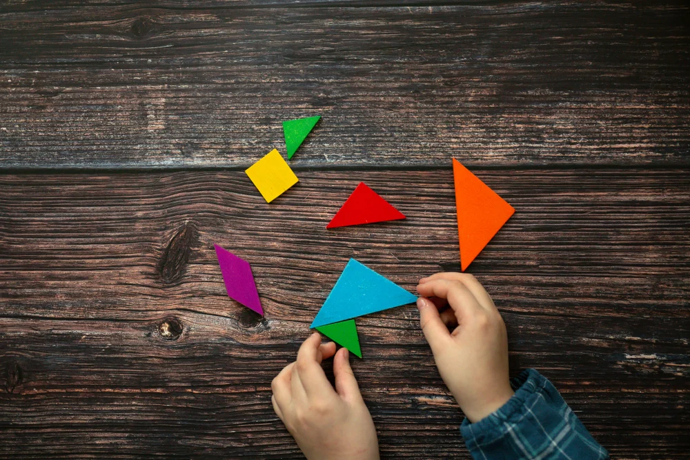 children's hands and wooden tangram game on a wooden background