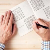 man solving sudoku puzzle on wooden office desk
