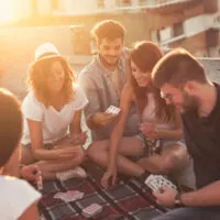 people sitting on a picnic blanket, having fun while playing cards